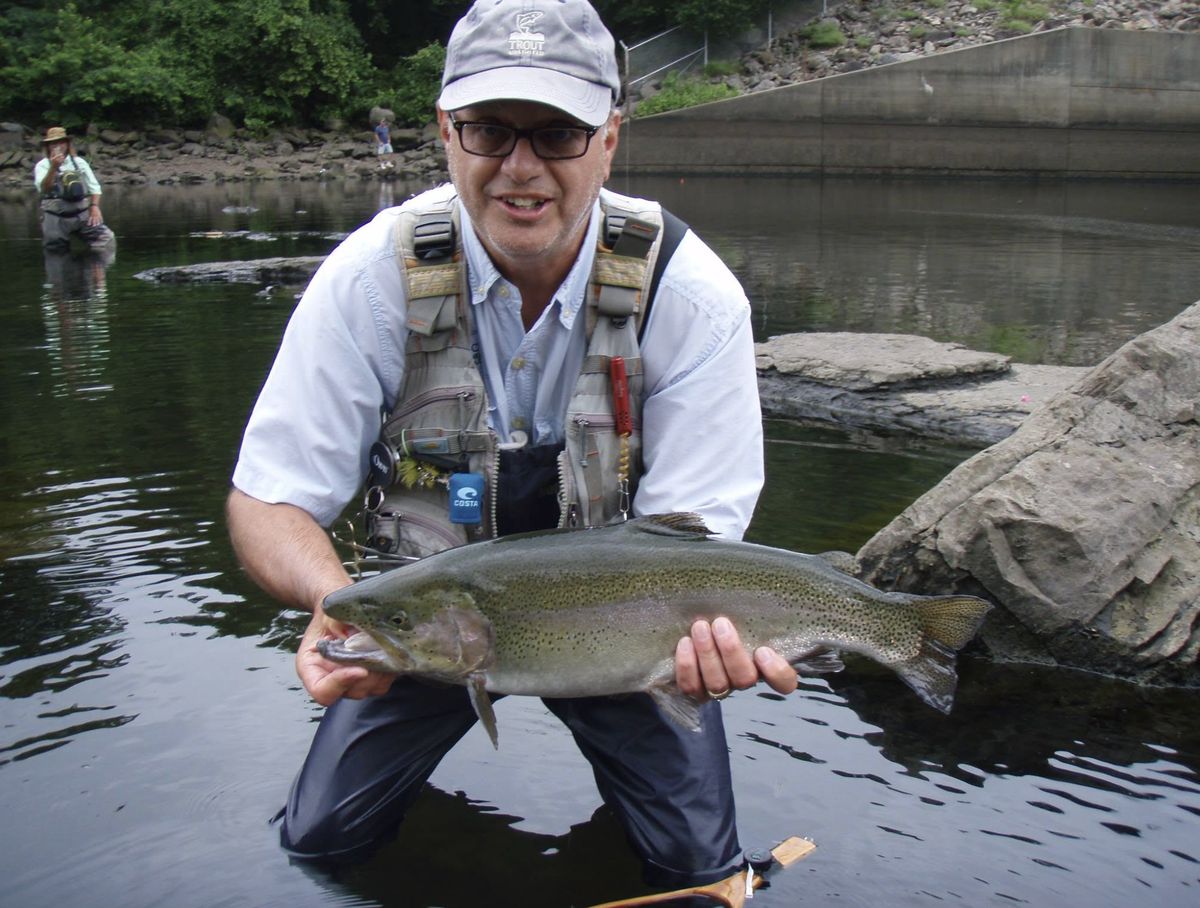 Scott Hood kneeling in the river holding a large rainbow trout