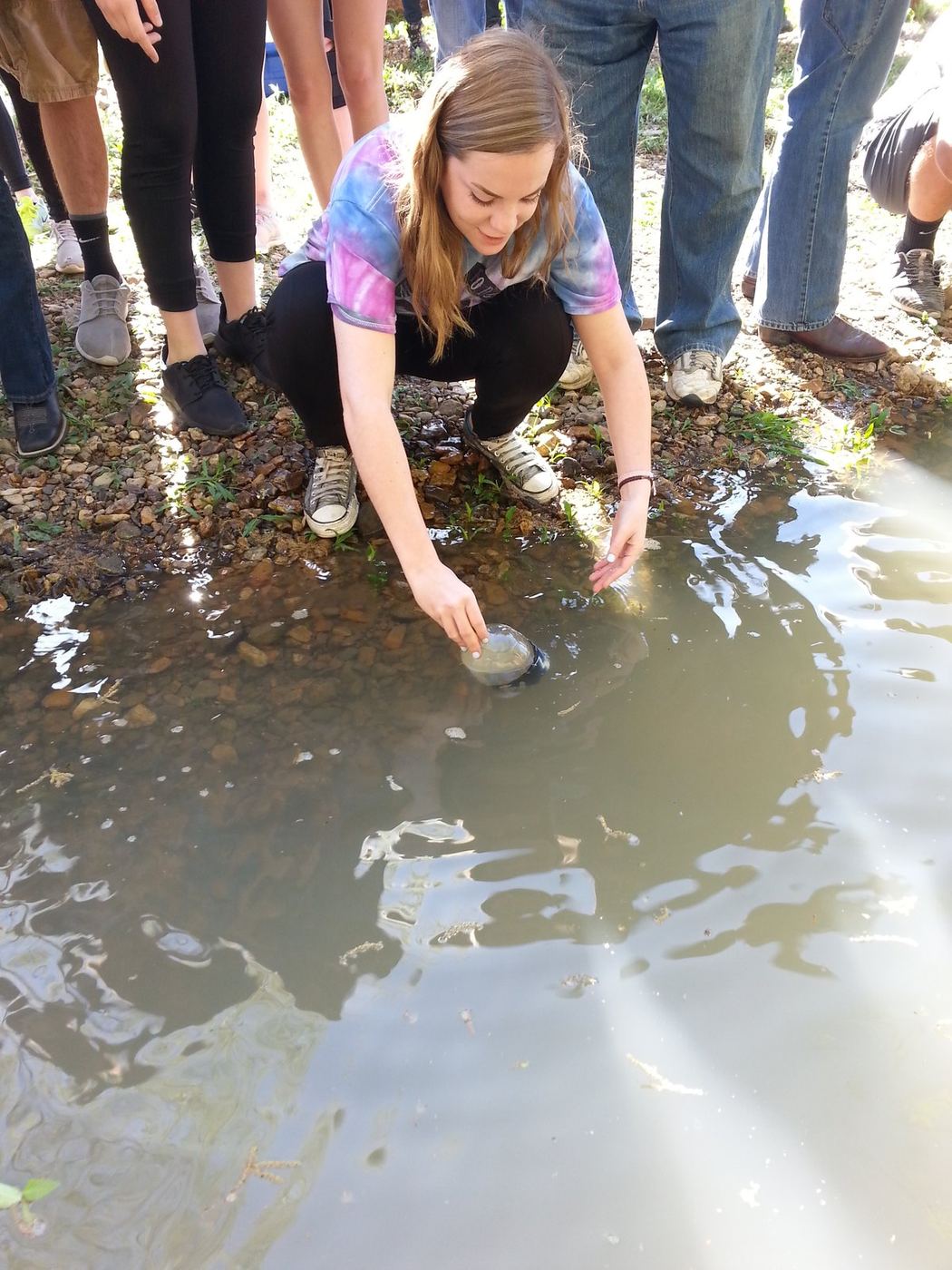 A student kneeling at the river's edge, releasing her trout